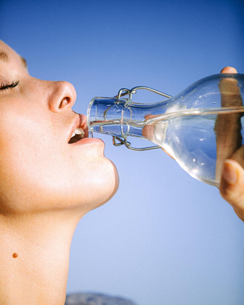 Frau beim achtsamen Wasser trinken aus einer Glasflasche vor blauem Himmel